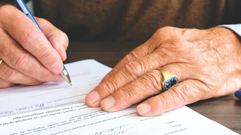 This article is about who pays closing costs in Broward County Florida. The image is of an older man signing a contract.